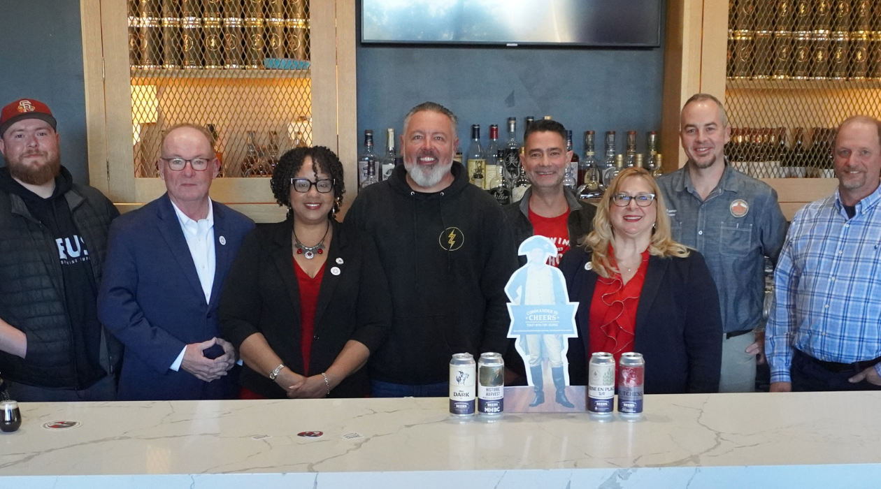 many people stand behind the marble bar at Zeus Brewing Company in Poughkeepsie with a small cardboard cutout of George Washington alongside four limited edition beer cans